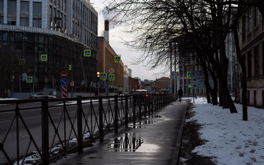 Ciemne stalowe ogrodzenie segmentowe ciągnie się wzdłuż krawędzi chodnika i oddziela go od mokrej jezdni w mieście zimą