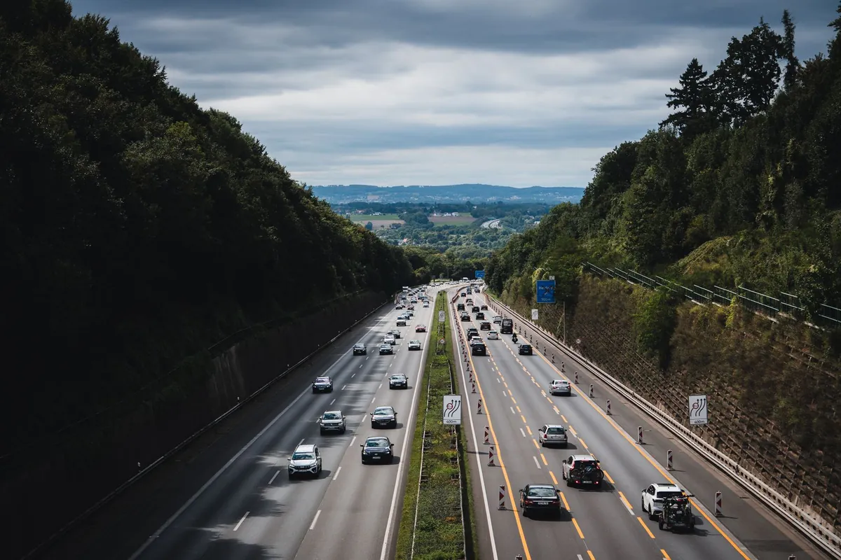 Autostrada w wykopie między zalesionymi zboczami, z barierami stalowymi w wąskim pasie dzielącym i przy murach oporowych po obu stronach