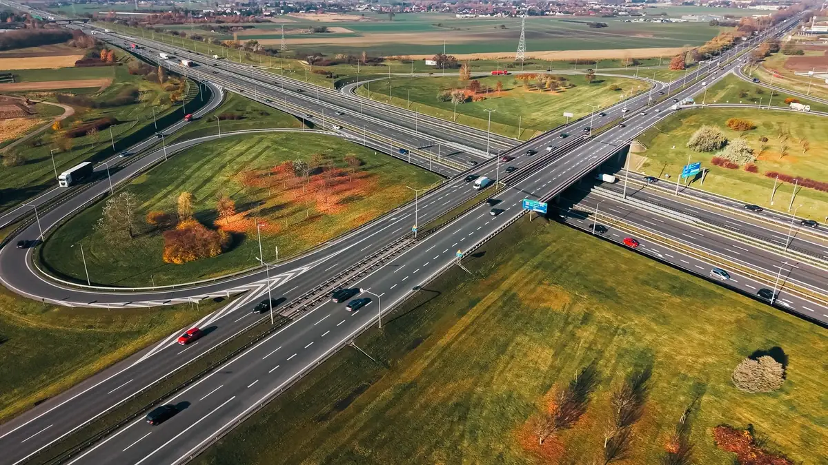 Węzeł drogowy z lotu ptaka: wiadukt, łącznice w kształcie pętli i dwie wielopasowe jezdnie wśród jesiennych pól