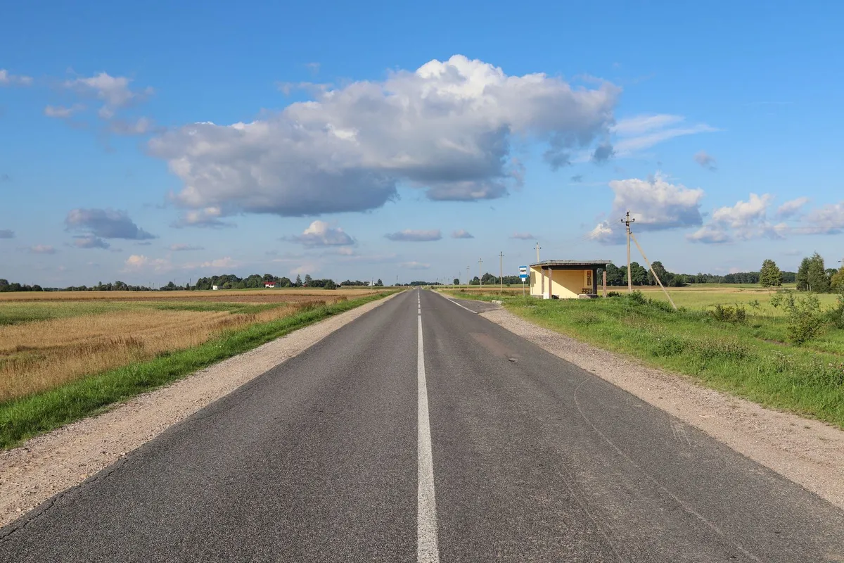 Prosta asfaltowa droga zamiejska z linią środkową, wiata przystankowa i pola po obu stronach