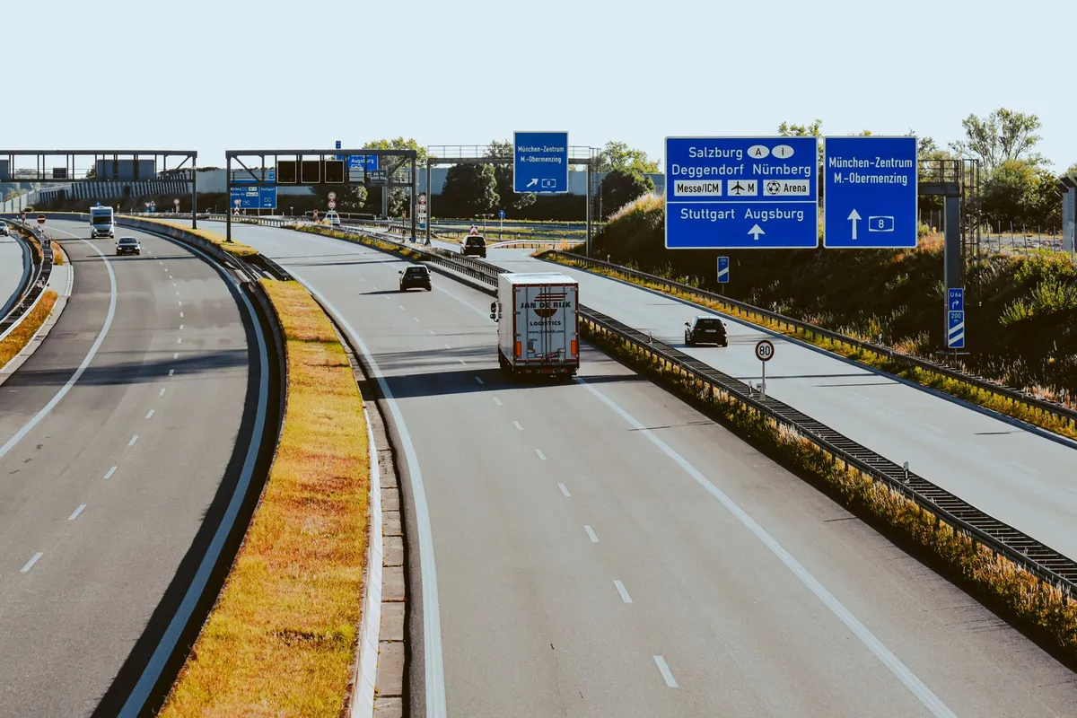 Autostrada w Niemczech z kilkoma kratownicowymi bramownicami, na których wiszą niebieskie drogowskazy i czarne tablice zmiennej treści