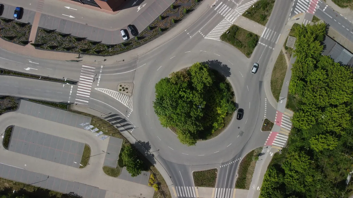 Jednopasowe rondo z zieloną wyspą środkową widziane z drona, z przejściami dla pieszych i przejazdami dla rowerów na wlotach