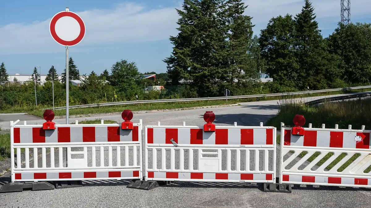 Biały okrągły znak z czerwoną obwódką nad czerwono-białymi zaporami z lampami ostrzegawczymi, które zamykają drogę