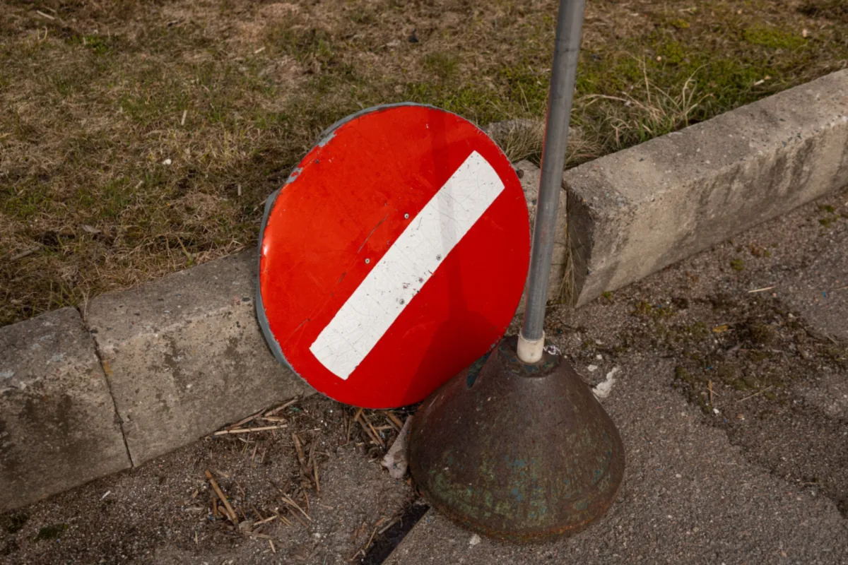 Odkręcona tarcza znaku zakazu wjazdu oparta o krawężnik obok pustego słupka na żeliwnej podstawie