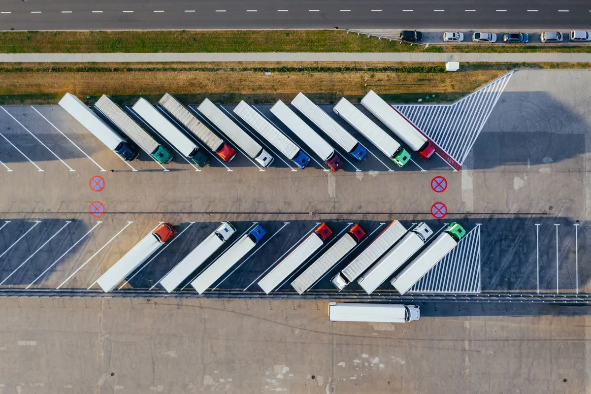 Plac postojowy z lotu ptaka: dwa rzędy ciągników siodłowych z białymi naczepami ustawionych ukośnie na wyznaczonych stanowiskach przy drodze