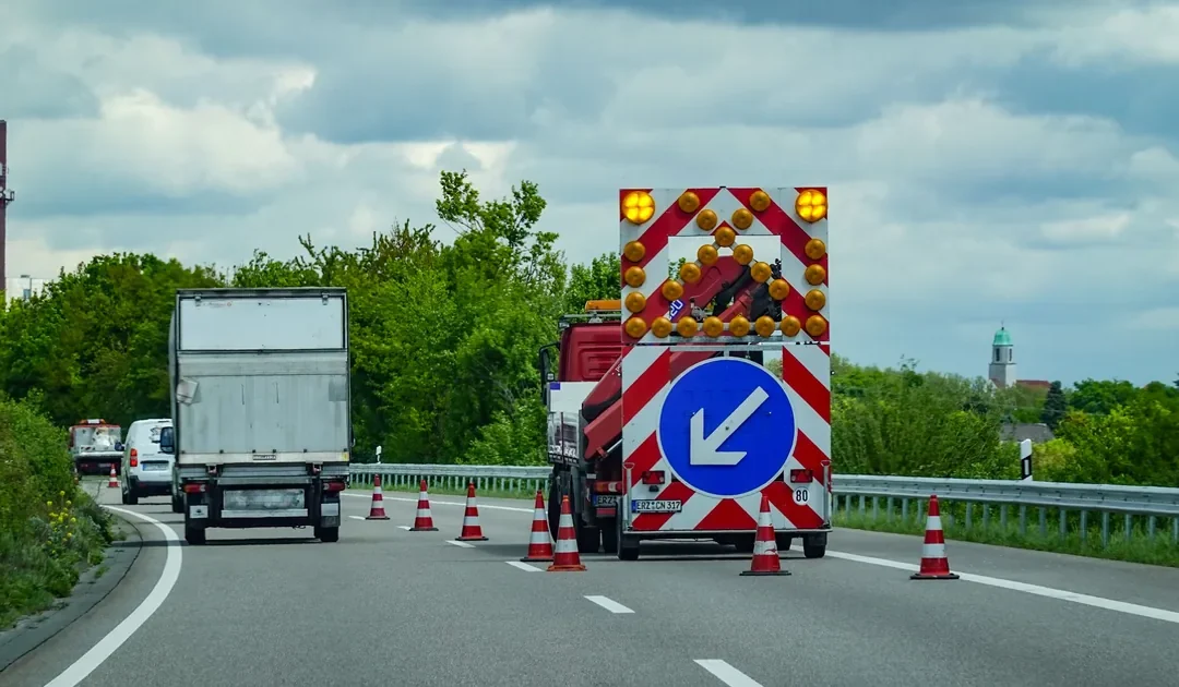 Roboty drogowe na drodze ekspresowej z pachołkami i tablicą kierującą na pojeździe