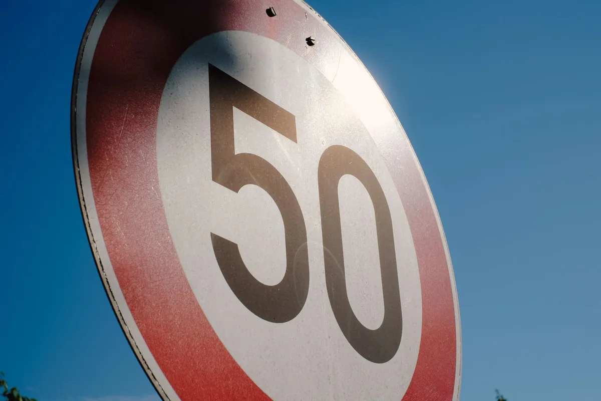 Okrągły znak ograniczenia prędkości do 50 km/h z czerwonym obramowaniem na tle błękitnego nieba