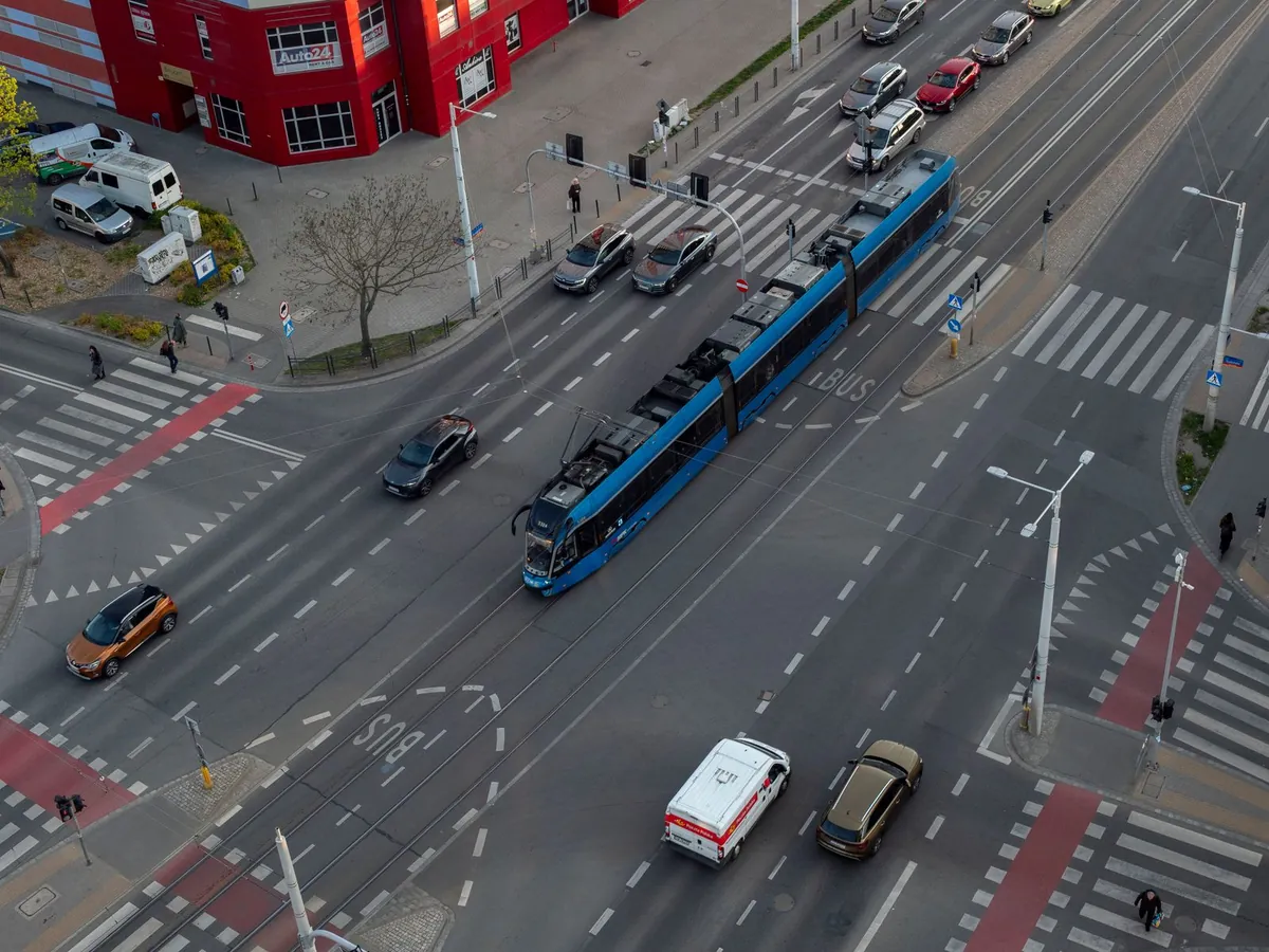 Widok z góry na skrzyżowanie we Wrocławiu z tramwajem, przejściami dla pieszych, czerwonymi przejazdami dla rowerzystów, liniami z trójkątów i napisem BUS na pasie