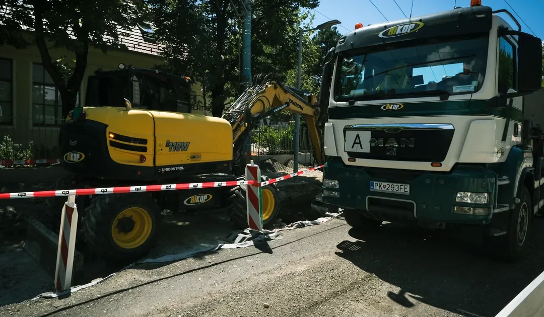Wykop w ulicy ogrodzony taśmą, obok koparka i samochód ciężarowy