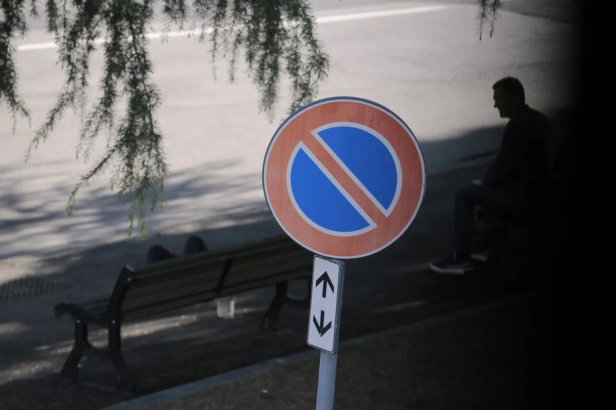 Znak zakazu postoju z jednym czerwonym skosem i tabliczką ze strzałkami w górę i w dół przy ławce w parku