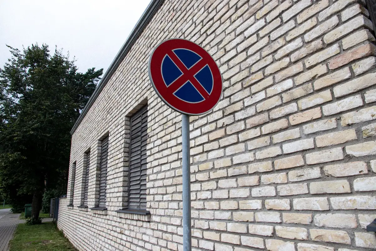 Okrągły znak zakaz zatrzymywania się z dwoma czerwonymi skosami na niebieskim tle przy ceglanym budynku