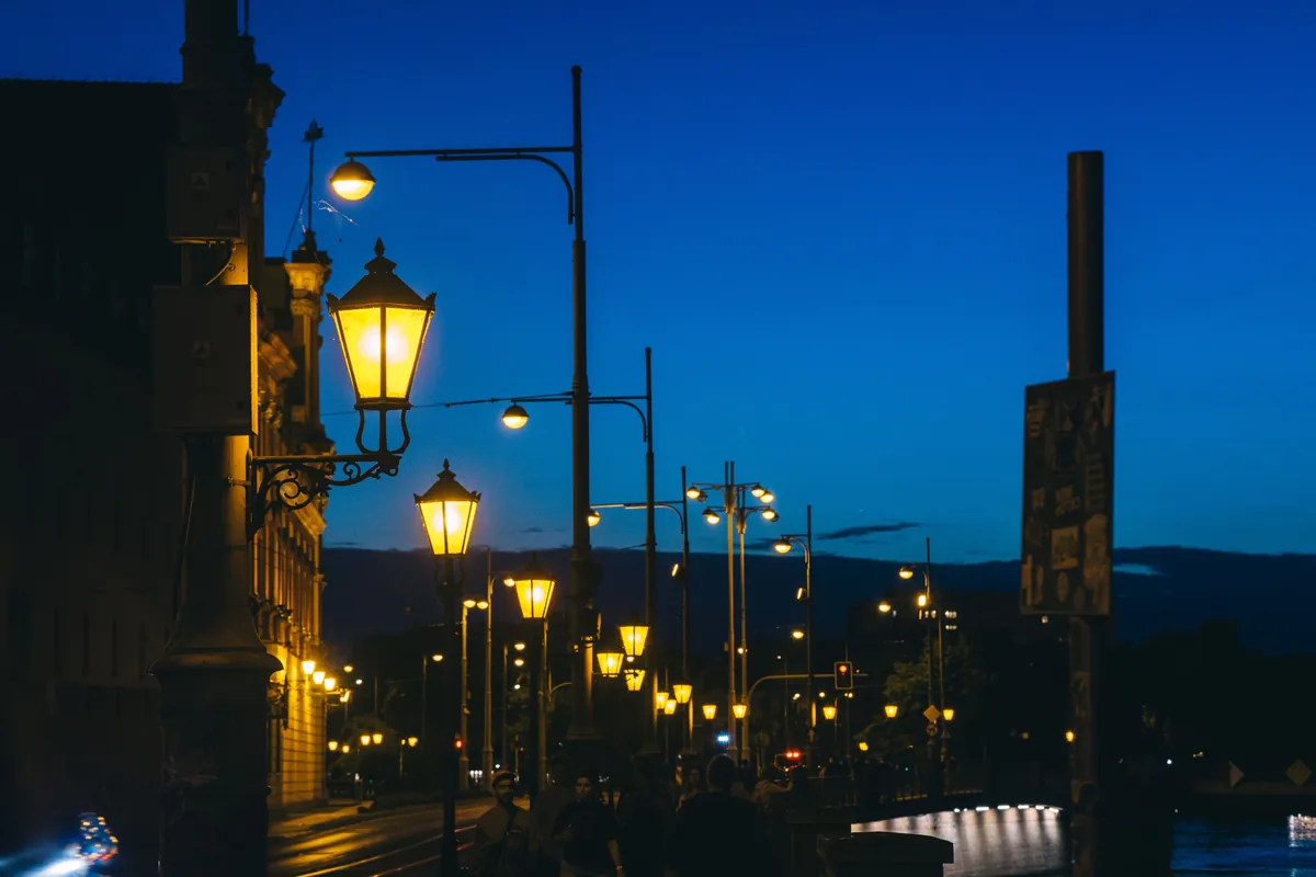 Ulica we Wrocławiu o zmierzchu z rzędem świecących latarni stylizowanych i nowoczesnych lamp drogowych na wysięgnikach